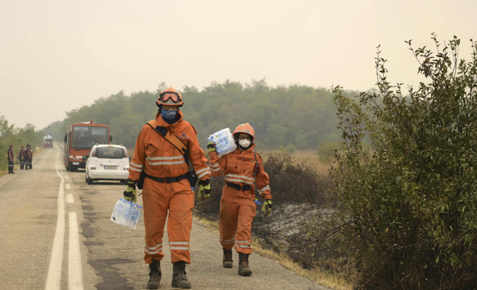 Firefighters carry bottles of water during a wildfire in Giannouli village, in the northeastern Evros region, Greece, Thursday, Aug. 31, 2023. Greek authorities have further reinforced firefighting forces in the country's northeast, where a massive blaze in its thirteenth day has flared up once more, triggering authorities to issue alerts to residents in the area to be on standby for possible evacuation. (e-evros.gr via AP)