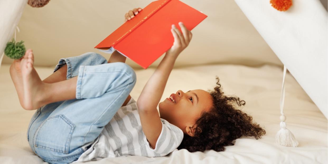 child reading a book in a fort - tips for raising readers