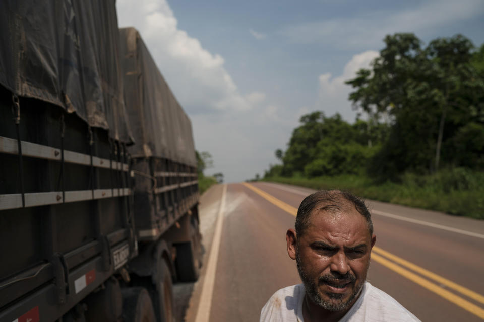 In this Nov. 28, 2019 photo, Lauzenir Araujo stands beside his truck after removing a layer of rubber from a damaged tire on route BR-163 near Ruropolis, Para state, Brazil. Araujo, who is hauling a load of manure to a grain plantation in the state of Mato Grosso, says that the old tires tend to explode as the truck can move faster on the newer road. "Eighty percent of your life is on the road," he says. "There is no life. That's why I say, this is for those who like it." (AP Photo/Leo Correa)