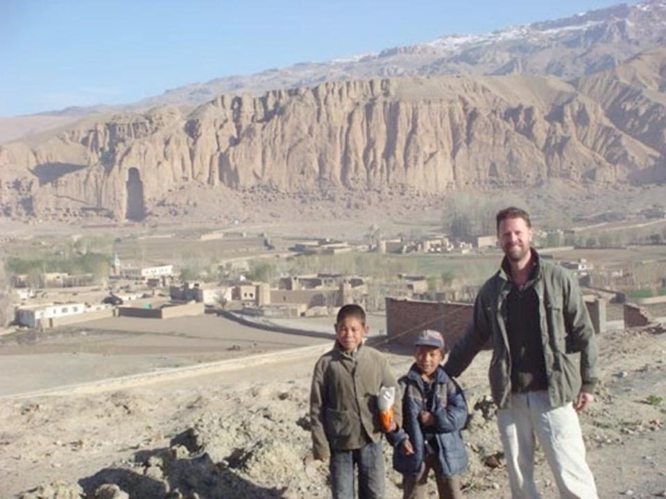 A man and two boys stand in front of cliffs showing a large void where a Buddha statue used to be