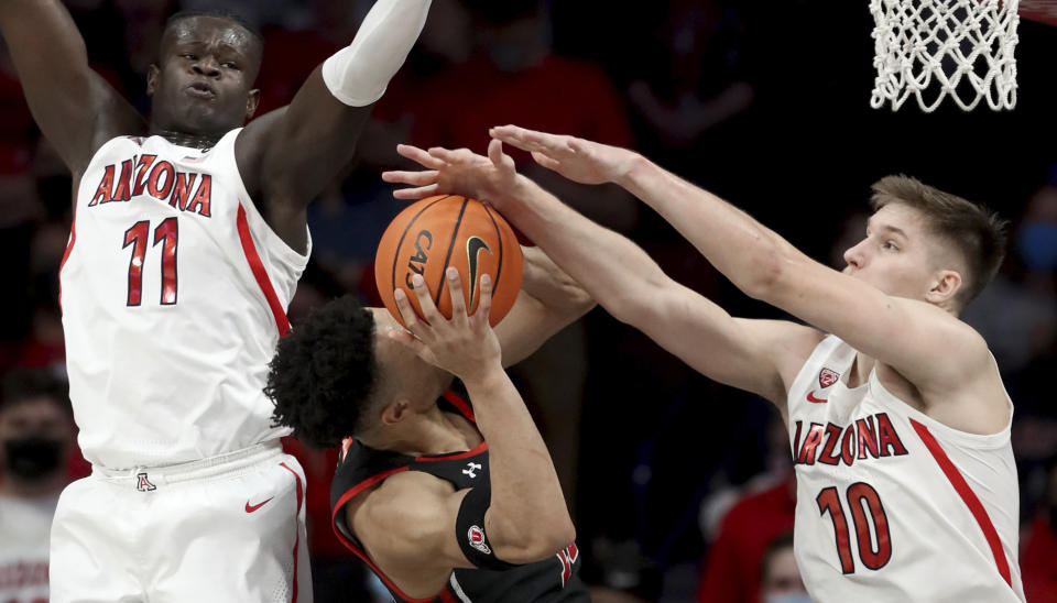 Arizona Wildcats center Oumar Ballo (11), left, and forward Azuolas Tubelis (10) stop Utah guard Marco Anthony's (10) drive to the basket in the second half of an NCAA college basketball game in Tucson, Ariz., Saturday, Jan. 15, 2022. (Kelly Presnell/Arizona Daily Star via AP)