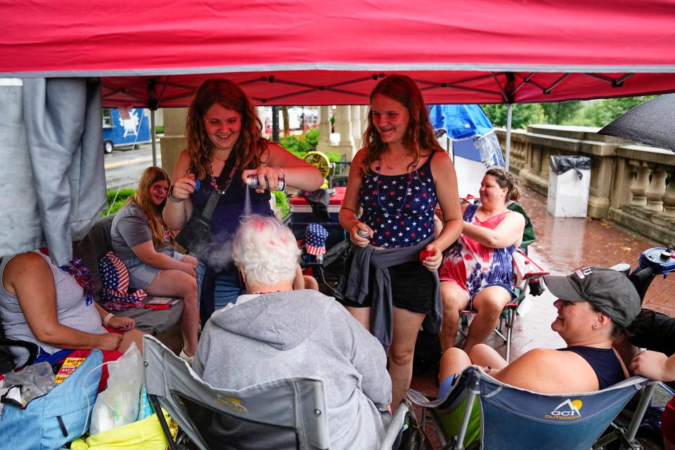 Marilyn Clap, 71, of Howard, Ohio, sits under a picnic umbrella as her granddaughters, Brooke Manning, 14, left, and Teagan Bowermaster, 12, spray red and blue dye stripes in her hair as rain falls in Downtown Columbus prior to Monday's Red, White & Boom activities.