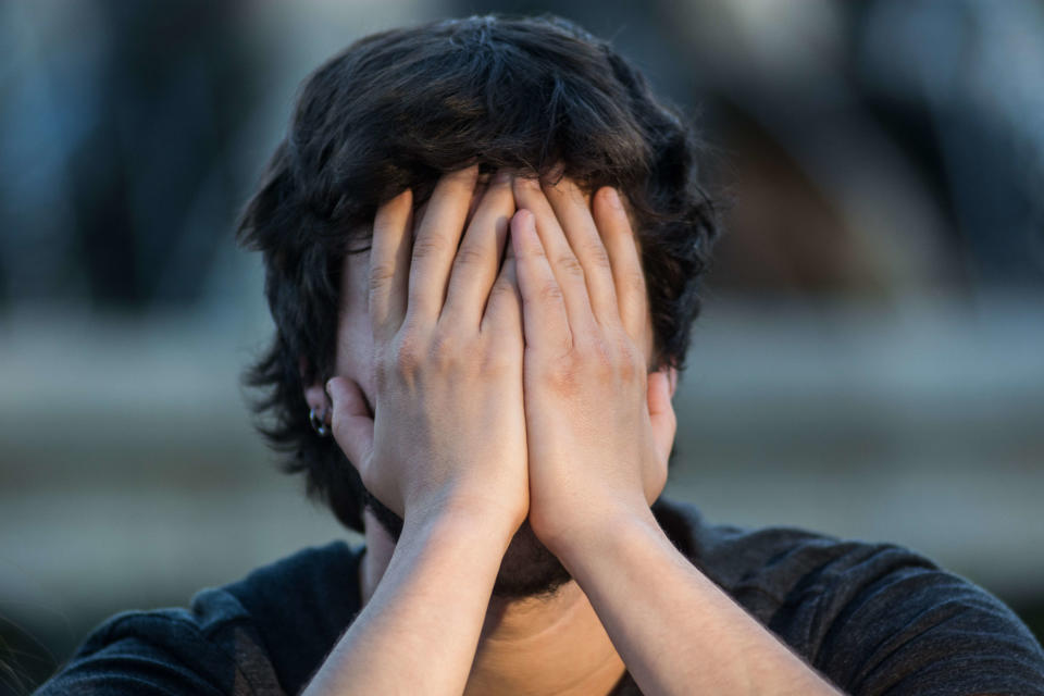 Person with hands covering their face, appearing distressed or overwhelmed outdoors