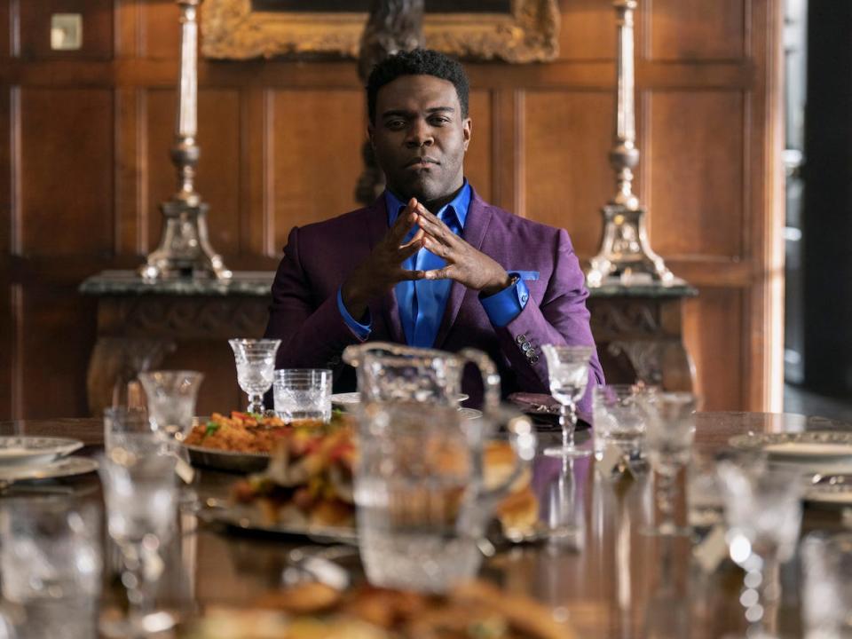 sam richardson in ted lasso, wearing a purple jacket and blue shirt and sitting in front of a lavish table
