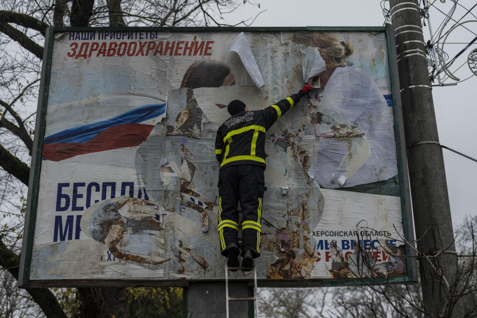 A Ukrainian firefighter tears off a Russian billboard in Kherson, southern Ukraine, Thursday, Nov. 17, 2022. (AP Photo/Bernat Armangue)