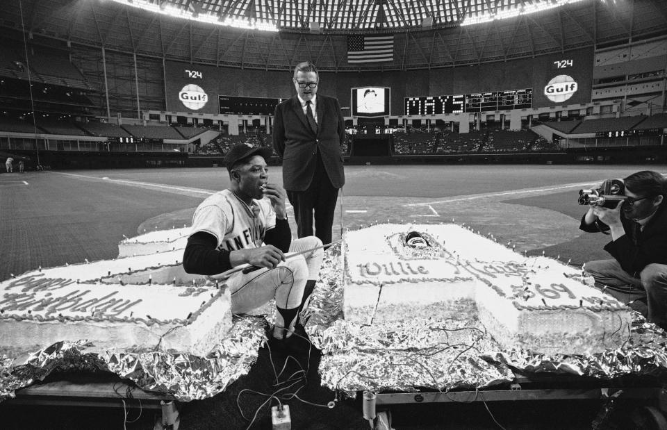 FILE - San Francisco centerfielder Willie Mays licks his fingers in centerfield after cutting the birthday cake given to him by Judge Roy Hofheinz, standing, in celebration of his 37th birthday before a baseball game against the Houston Astros in Houston, Texas, in this May 6, 1968, file photo. The 569 pound cake, one pound for each of Mays home runs, contains 3,800 eggs, 150 pounds of butter, 150 pounds of sugar, 300 pounds of flour, and 100 pounds of almonds. The cake is in the figure of 24, Mays uniform number. Mays turns 90 on Thursday, May 6, 2021. (AP Photo/Ed Kolenovsky, File)