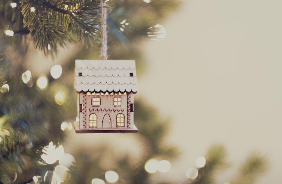 An illuminated house ornament is hanging from a decorated Christmas tree. mortgages