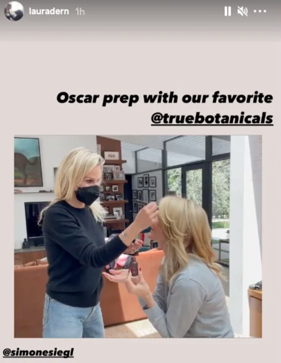 Laura dern holds up a bottle of true botanics oil while her makeup artist finishes her Oscars look