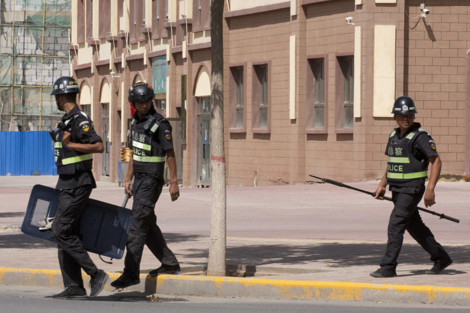 FILE - In this Aug. 31, 2018, file photo, policemen patrol past a building's wall mounted with surveillance cameras in Peyzawat, western China's Xinjiang region. The Chinese database Victor Gevers found online was not just a collection of old personal details. The discovery by Gevers, a Dutch cybersecurity researcher who revealed it on Twitter last week, has given a rare glimpse into China’s extensive surveillance of Xinjiang, a remote region home to an ethnic minority population that is largely Muslim. The area has been blanketed with police checkpoints and security cameras that apparently are doing more than just recording what happens. The database Gevers found appears to have been recording people’s movements tracked by facial recognition technology, he said, logging more than 6.7 million coordinates in a span of 24 hours. (AP Photo/Ng Han Guan, File)