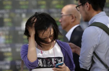 A pedestrian looks at her mobile phone as a strong wind caused by tropical storm Vongfong blows while she stands in front of an electronic board showing various stock prices outside a brokerage in Tokyo October 14, 2014. REUTERS/Yuya Shino