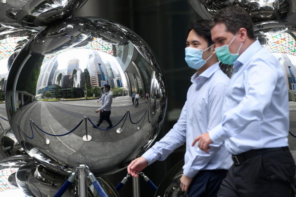 Men wearing face masks walk past an art installation in the financial business district in Singapore on August 11, 2020. - Singapore's virus-hammered economy shrank almost 43 percent in the second quarter, in a sign that the country's first recession in more than a decade was deeper than initially estimated, official data showed on August 11. (Photo by Roslan RAHMAN / AFP) (Photo by ROSLAN RAHMAN/AFP via Getty Images)