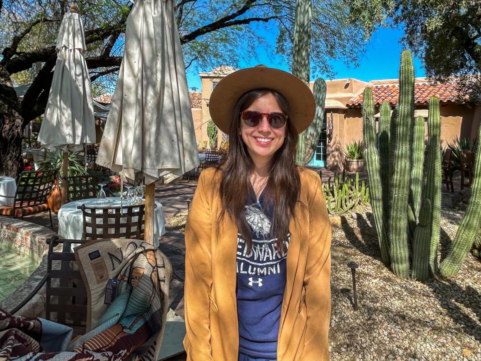 The author in a cowboy hat and sunglasses stands smiling in front of cacti and an adobe building in Scottsdale