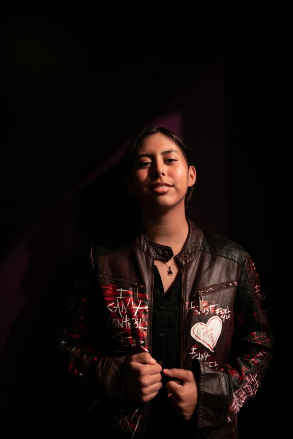 A teenage girl leans up against a black wall.