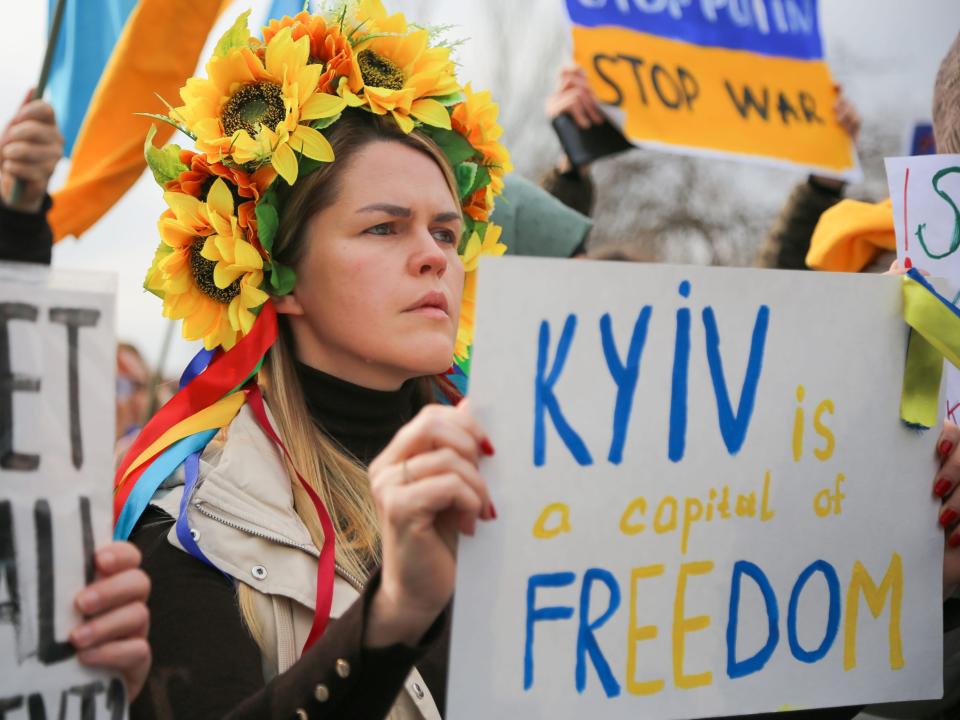 A woman wearing a sunflower flower crown holds a sign that says "Kyiv is a capital of freedom."