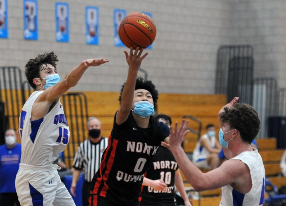 North Quincy's Ethan Gao, center, underhands a shot past Quincy defenders Will Cook, left, and Joseph Manton, right, during boys basketball action at Quincy High School, Tuesday, Jan. 19, 2021.