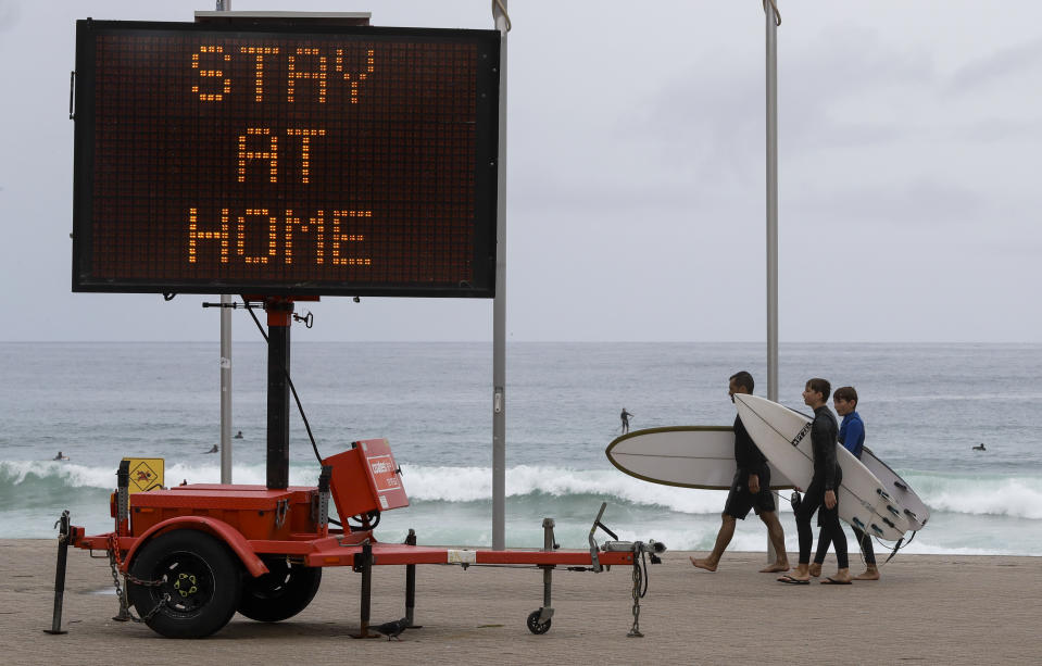 Surfers carry their boards along the beach front at Manly on the northern beaches in Sydney, Australia, Monday, Dec. 21, 2020. Sydney's northern beaches are in a lockdown similar to the one imposed during the start of the COVID-19 pandemic in March as a cluster of cases in the area increased to more than 80. (AP Photo/Mark Baker)