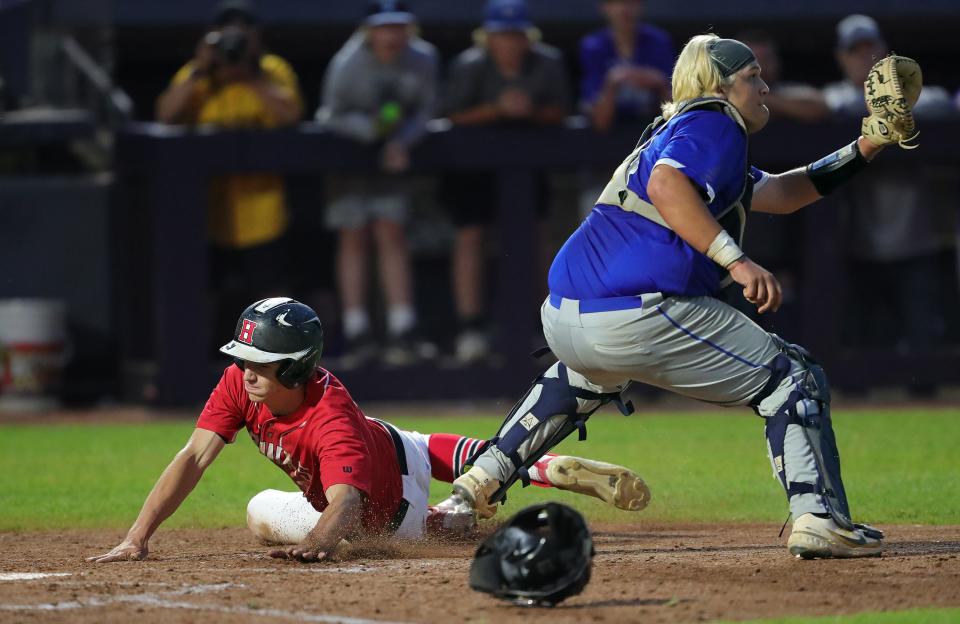 Hiland baserunner Colin Coblentz, left, dives past Calvert catcher Connor Moyer to score the game-tying run during the seventh inning of an OHSAA Division IV state semifinal baseball game at Canal Park, Thursday, June 8, 2023, in Akron, Ohio.