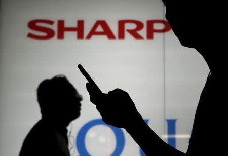 A man using his mobile phone walks past a logo of Sharp Corp outside an electronics shop in Tokyo, Japan, July 31, 2015. REUTERS/Yuya Shino