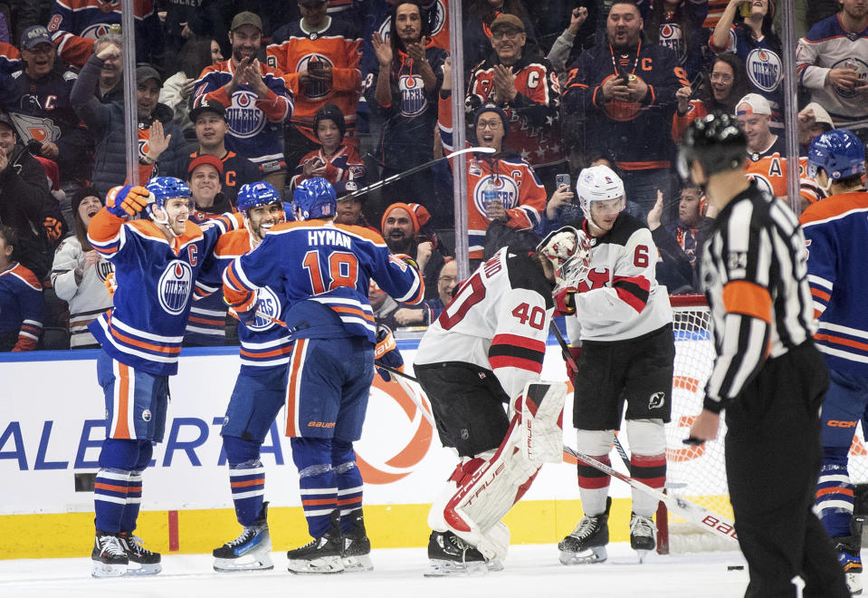 New Jersey Devils goalie Akira Schmid (40) and John Marino (6) react as Edmonton Oilers' Connor McDavid (97), Evander Kane (91) and Zach Hyman (18) celebrate after a goal during third-period NHL hockey game action in Edmonton, Alberta, Sunday, Dec. 10, 2023. (Jason Franson/The Canadian Press via AP)