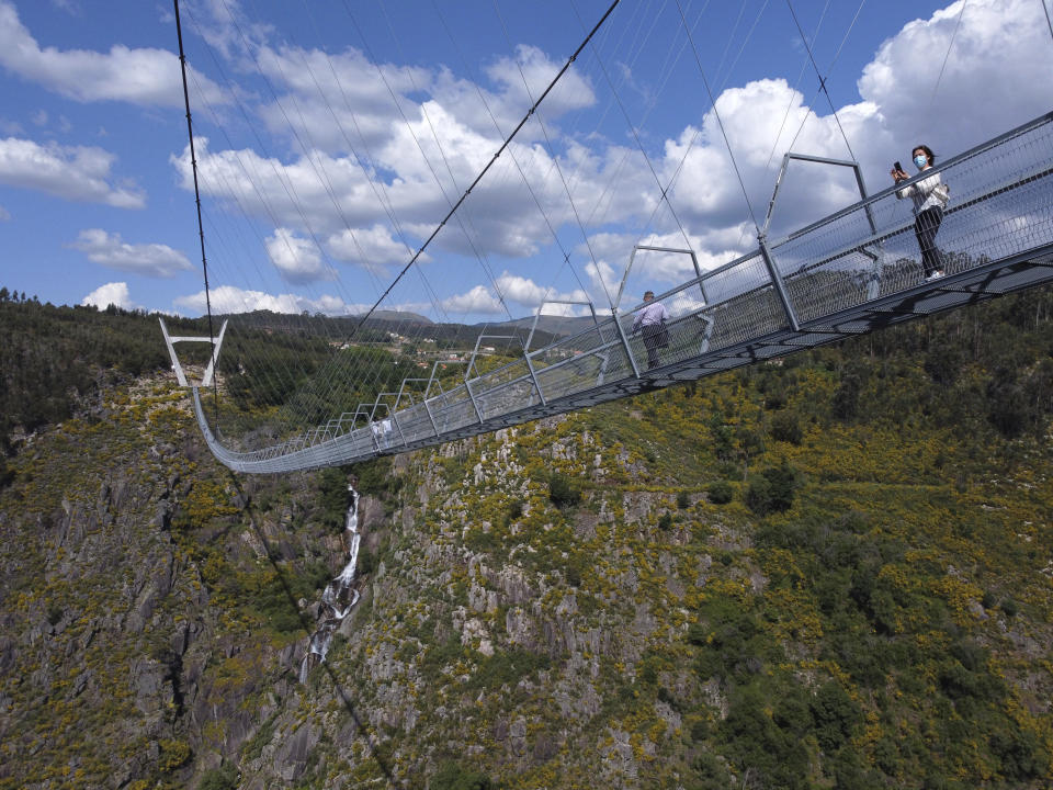 People walk across a narrow footbridge suspended across a river canyon, which claims to be the world's longest pedestrian bridge, in Arouca, northern Portugal, Sunday, May 2, 2021. The Arouca Bridge inaugurated Sunday, offers a half-kilometer (almost 1,700-foot) walk across its span, some 175 meters (574 feet) above the River Paiva. (AP Photo/Sergio Azenha)