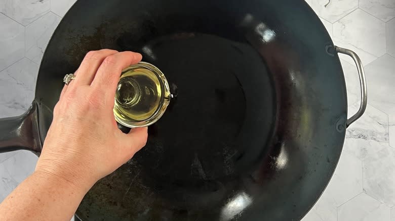 hand pouring oil in wok