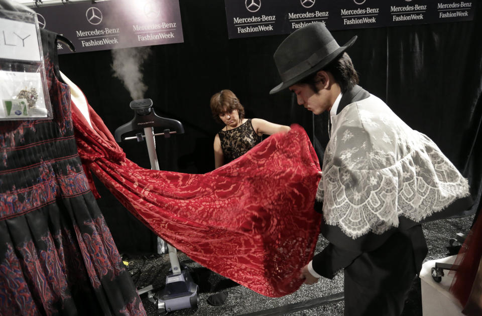 Workers steam one of the dresses of designer Tadashi Shoji backstage before his Fall 2013 collection is modeled during Fashion Week in New York, Thursday, Feb. 7, 2013. (AP Photo/Richard Drew)