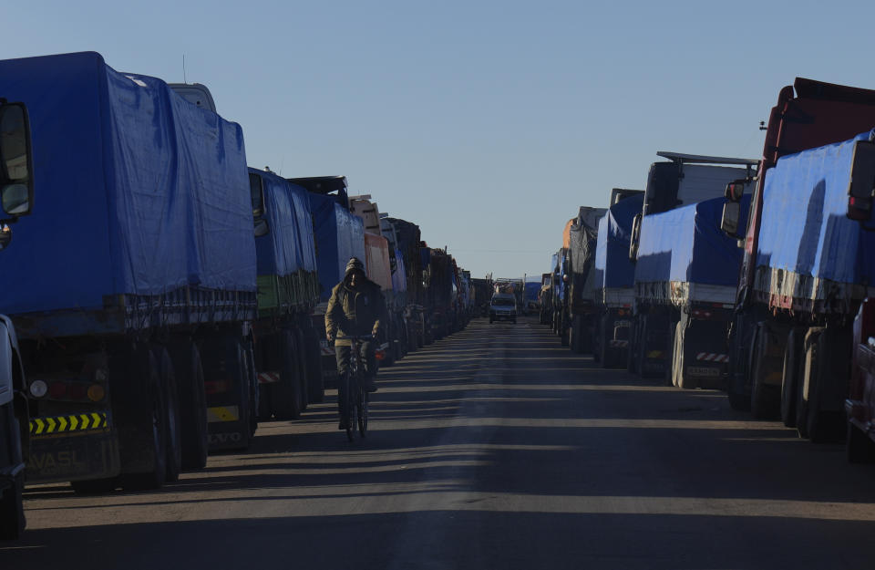 A cyclist rides past cargo trucks backed up in Desaguadero, Bolivia, on the border with Peru, unable to cross to Peru due to roadblocks by anti-government protests in Peru, Friday, Jan. 13, 2023. (AP Photo/Juan Karita)