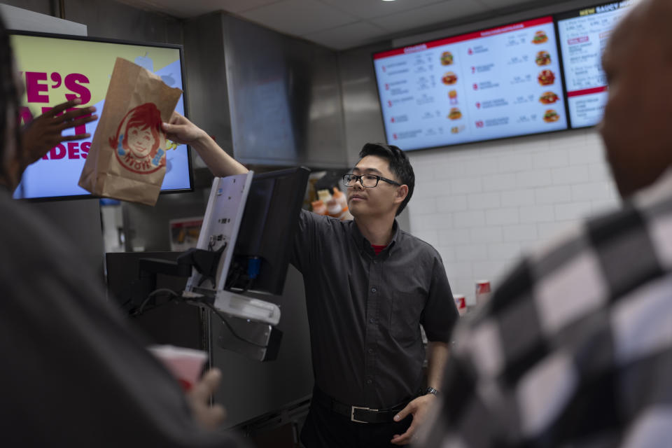 Lawrence Cheng, whose family owns seven Wendy's locations south of Los Angeles, hands an order to a customer at his Wendy's restaurant in Fountain Valley, Calif., June 20, 2024. When California’s minimum wage increase went into effect in April, fast food workers across the state went from making $16 to $20 overnight. It's already having an impact, according to local operators for major fast food chains, who say they are reducing worker hours and raising menu prices as the sudden increase in labor costs leaves them scrambling for solutions. (AP Photo/Jae C. Hong)