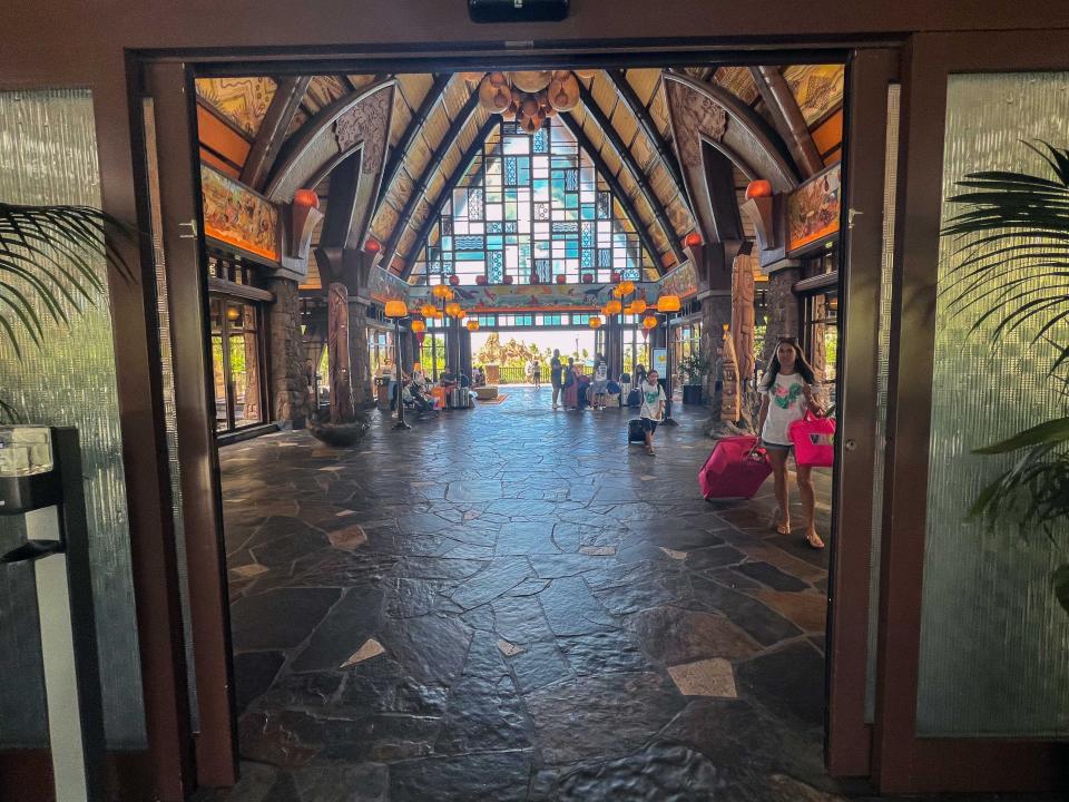 Entering the dramatic lobby at Aulani Disney resort with stone floors, stained glass, windows, and arched ceilings.