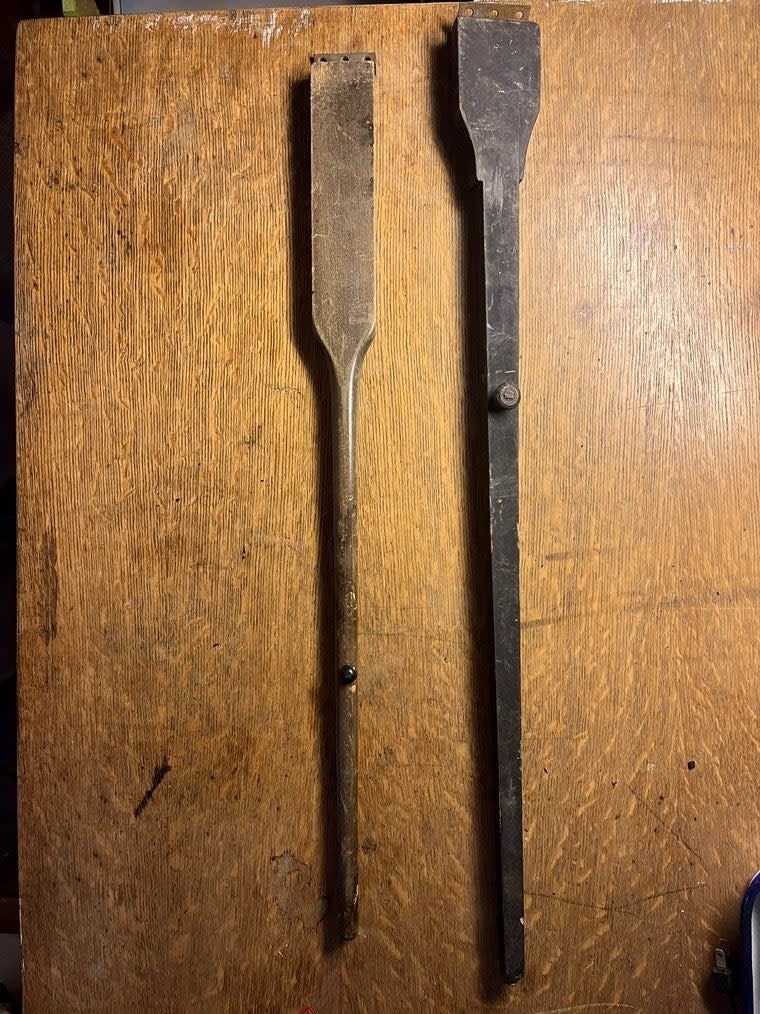 Two wooden spatulas, both showing signs of wear, on a wooden table. One oar has a screw at the end