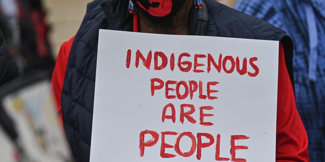 A participant holds a placard with words 'Indigenous People Are People.'