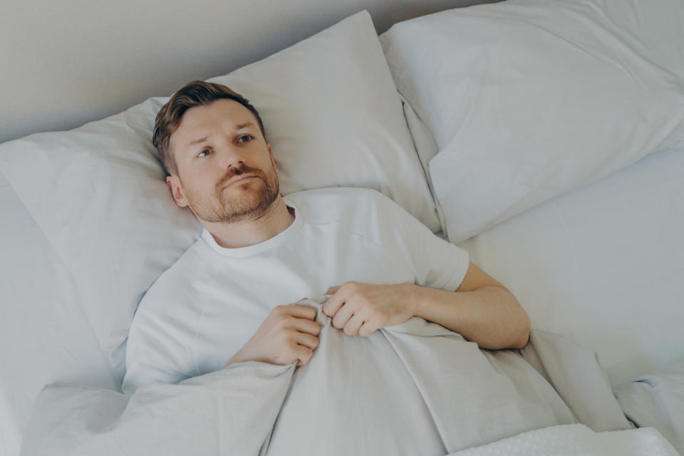 Person lying in bed under covers looking up, with an expression of contemplation or concern