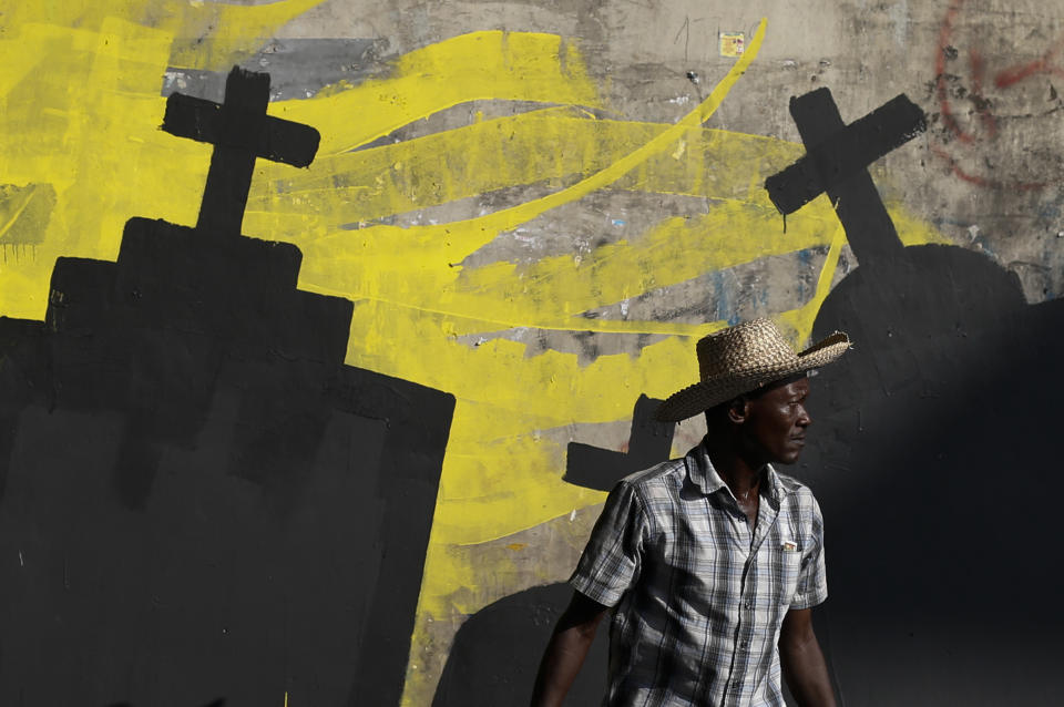 A man walks past a mural being painted by students from the National School of the Arts to express solidarity with those killed during a month of protests demanding the president's resignation in Port-au-Prince, Haiti, Tuesday, Oct. 15, 2019. President Jovenel Moïse broke his silence Tuesday and said it would be irresponsible for him to resign amid Haiti's unrest, which has entered a fifth week of deadly protests that have paralyzed the economy and shuttered schools. (AP Photo/Rebecca Blackwell)