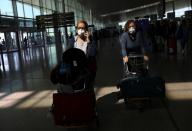 Passengers from Italy wear protective face masks as they walk with their luggage after cancelling the flights to Italy from Spain, after further cases of coronavirus were confirmed in Barcelona