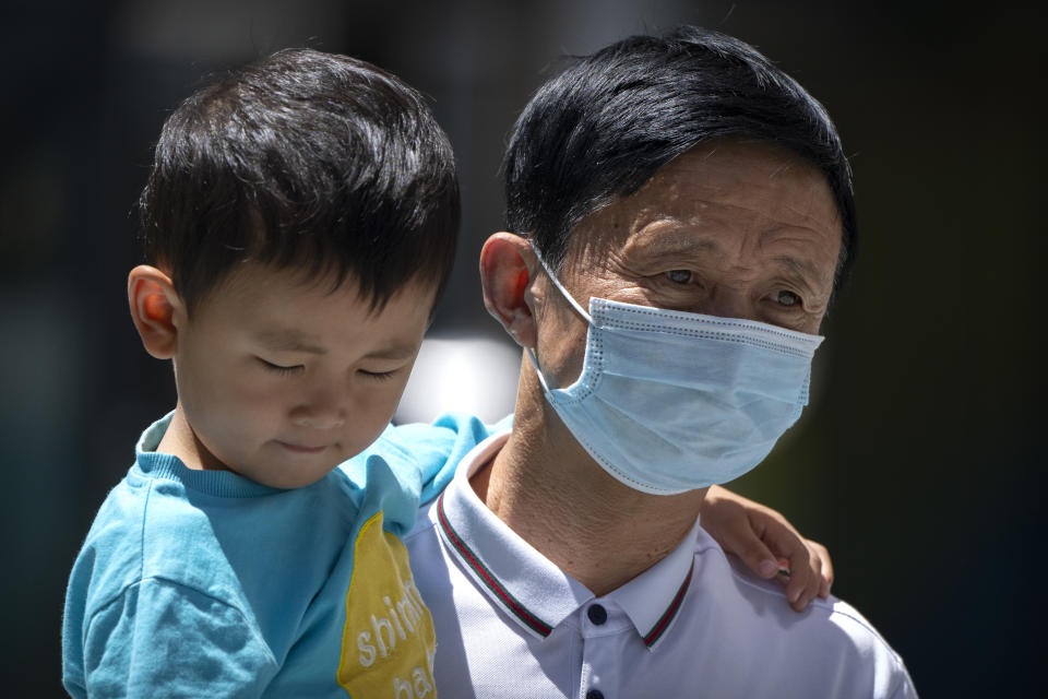 A man wearing a face mask to protect against COVID-19 carries a boy as they walk at a shopping and office complex in Beijing, Friday, May 28, 2021. (AP Photo/Mark Schiefelbein)