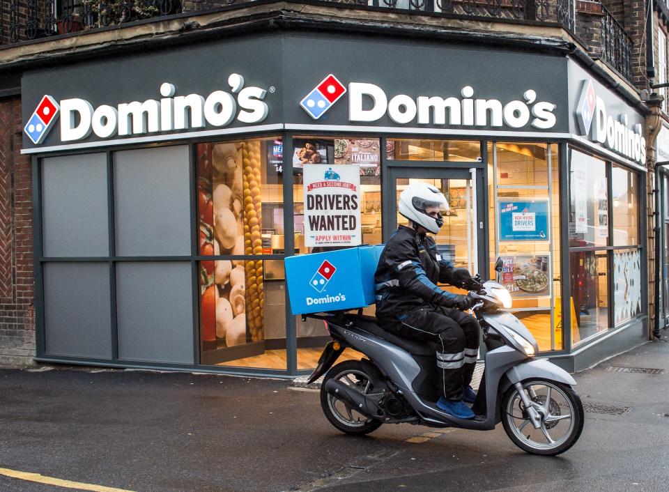 <p>A delivery rider outside a branch of Domino’s Pizza</p> (PA Media)