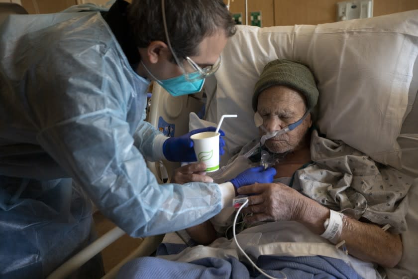 MISSION HILLS, CA - DECEMBER 29: Chaplain Kevin Deegan, left, gives Juan Legaspi-Lozano, 90, a small sip of water after checking with the nurse first at Providence Holy Cross Medical Center on Tuesday, Dec. 29, 2020 in Mission Hills, CA. Juan is a patient inside the covid unit (Francine Orr / Los Angeles Times)