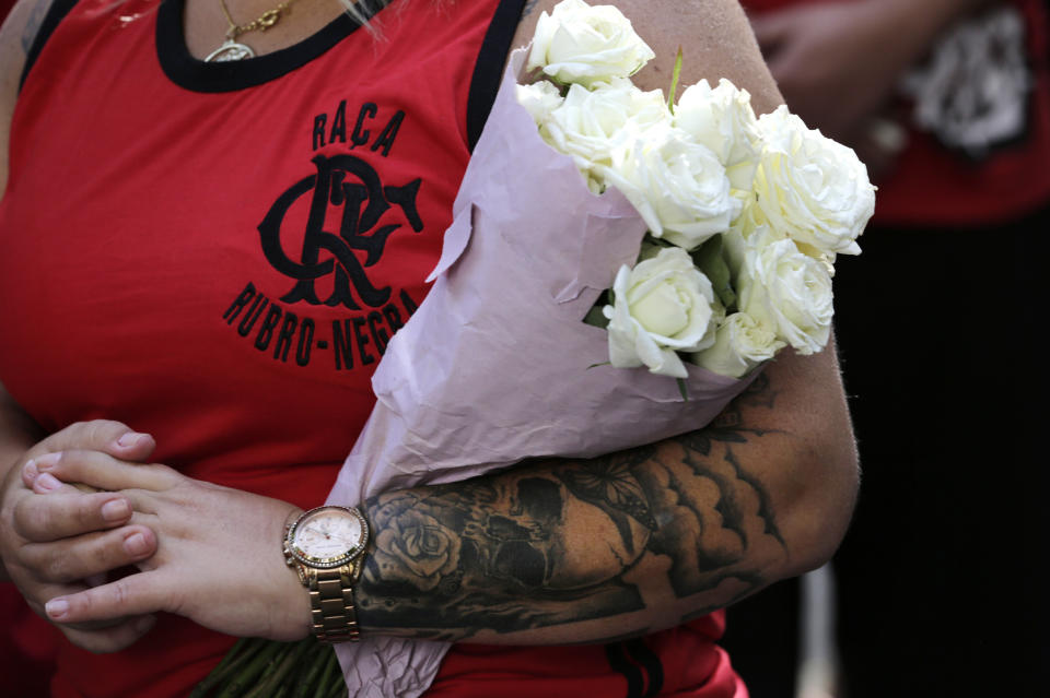 Flamengo soccer fan carries white flowers in honor of the teenage players killed by a fire, in Rio de Janeiro, Brazil, Saturday, Feb. 9, 2019. A fire early Friday swept through the sleeping quarters of an academy for Brazil's popular professional soccer club Flamengo, killing several and injuring others, most likely teenage players, authorities said. (AP Photo/Silvia Izquierdo)