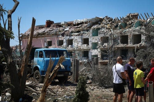 Local residents stand next to damaged residential building in the town of Serhiivka, located about 50 kilometers (31 miles) southwest of Odesa, Ukraine, Friday, July 1, 2022. Russian missile attacks on residential areas in a coastal town near the Ukrainian port city of Odesa early Friday killed at least 21 people, authorities reported, a day after Russian forces withdrew from a strategic Black Sea island. (AP Photo/Nina Lyashonok) ORG XMIT: XSG121