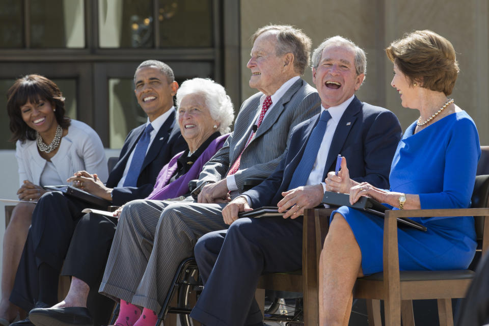 Former President George W. Bush laughs with his father, George H.W. Bush, at the dedication of the George W. Bush presidential library on the campus of Southern Methodist University on April 25, 2013, in Dallas. On the left are first lady Michelle Obama, President Barack Obama and former first lady Barbara Bush. On the right is former first lady Laura Bush.