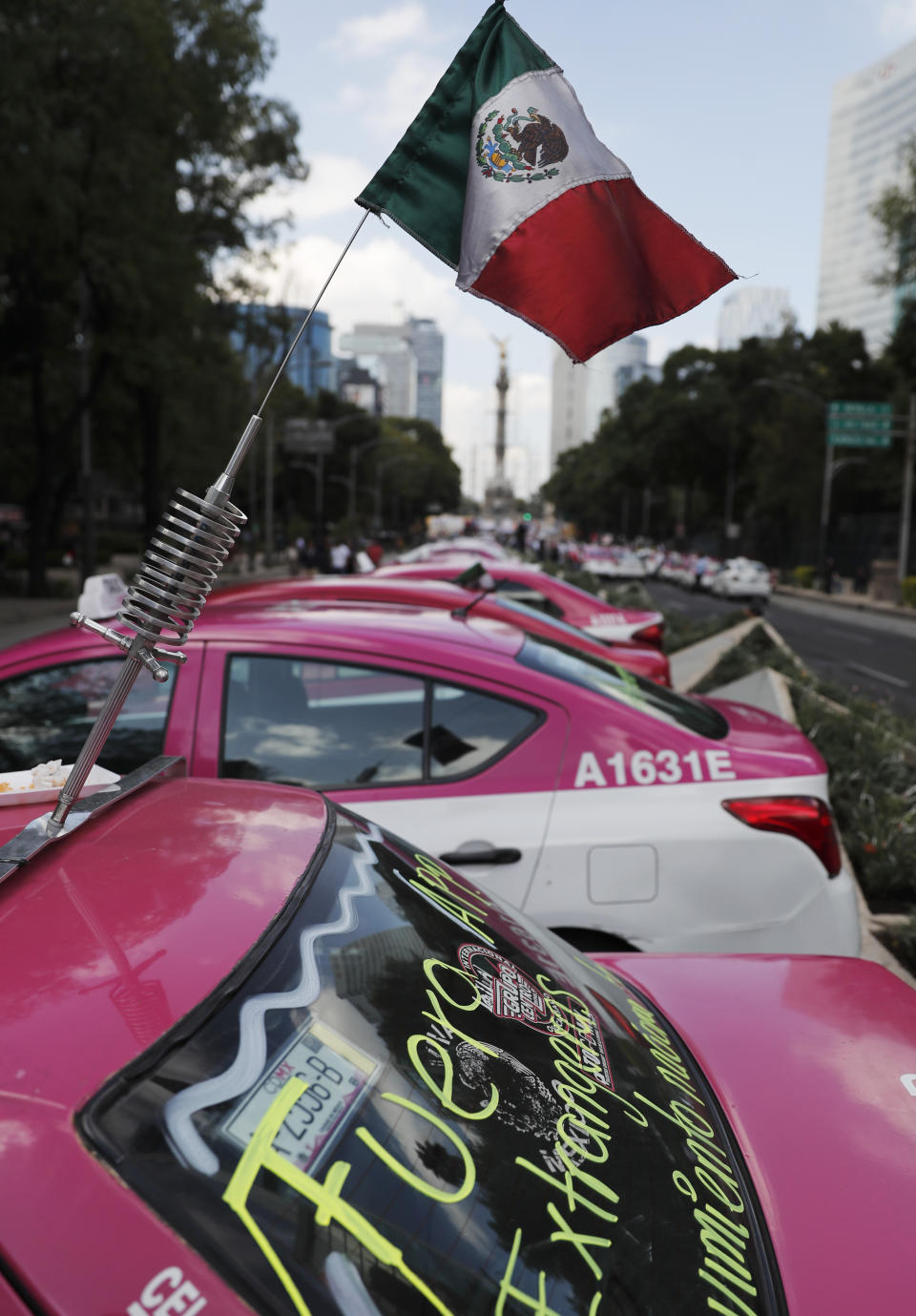 A Mexican national flag is displayed from an antenna as hundreds of taxi drivers gather to protest ride apps, in Mexico City, Monday, Oct. 7, 2019. The protesters want the apps banned, arguing that the apps are unfair competition because those drivers are more loosely regulated and don't have to pay licensing fees. (AP Photo/Marco Ugarte)