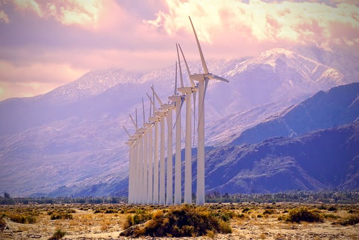 A row of wind turbines in the desert with a mountain in the background.