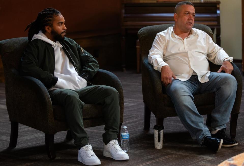 Two men sit side by side in armchairs.