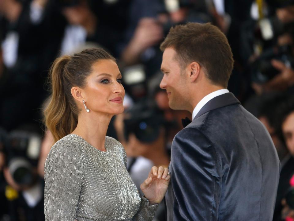 Gisele Bündchen in silver dress and Tom Brady in gray suit in front of crowd