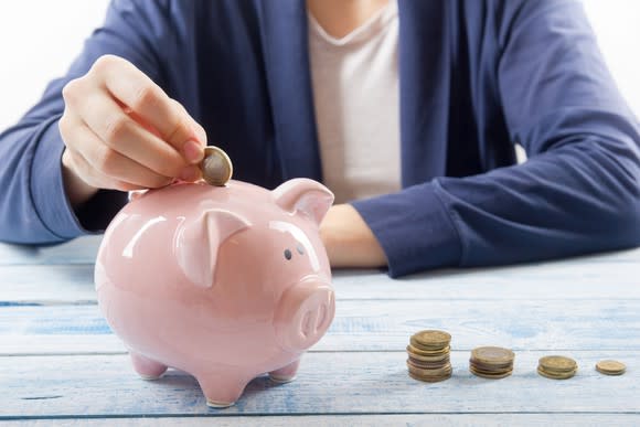 Child putting money into a piggy bank with stacks of coins nearby