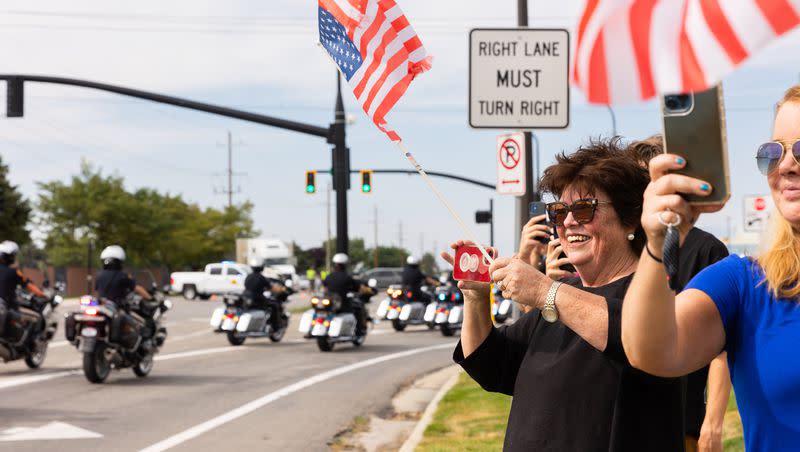 Kathy Stidham waves her American flag as the presidential motorcade drives out of the Roland R. Wright Air National Guard Base in Salt Lake City on Wednesday, Aug. 9, 2023.