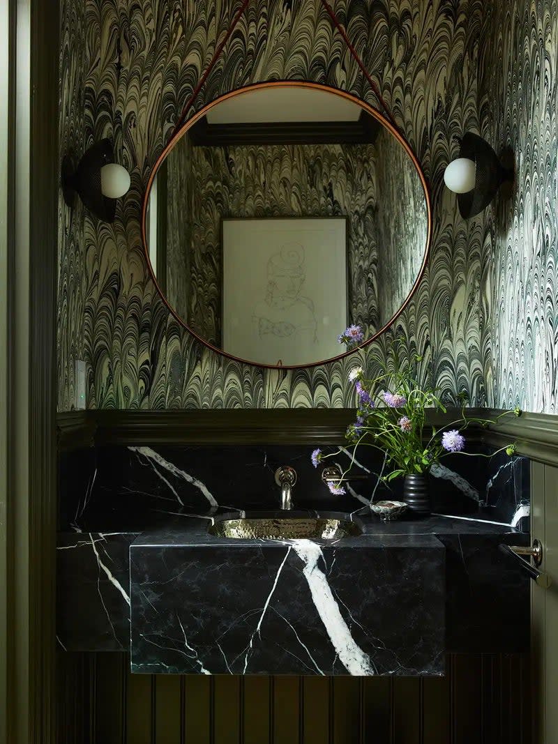 Bathroom with black stone vanity and marbled green wallpaper. 