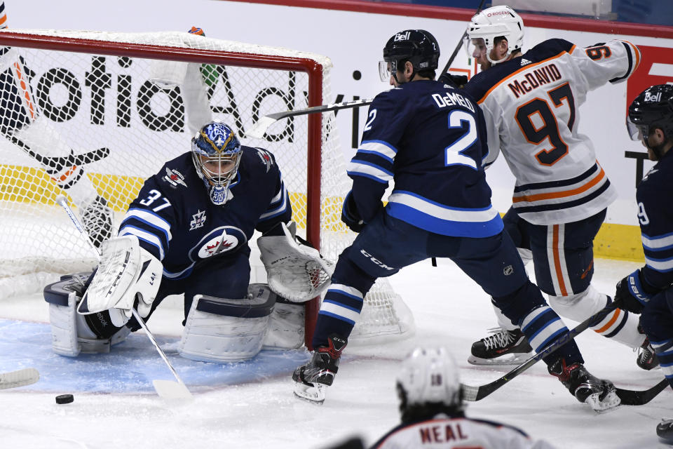 Winnipeg Jets goaltender Connor Hellebuyck (37) clears the puck as Dylan DeMelo (2) defends against Edmonton Oilers' Connor McDavid (97) during the first period of an NHL hockey game Tuesday, Jan. 26, 2021, in Winnipeg, Manitoba. (Fred Greenslade/The Canadian Press via AP)