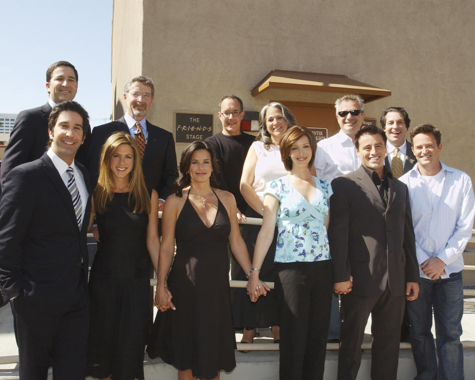 The Friends cast and executive producers smiling and standing together and smiling