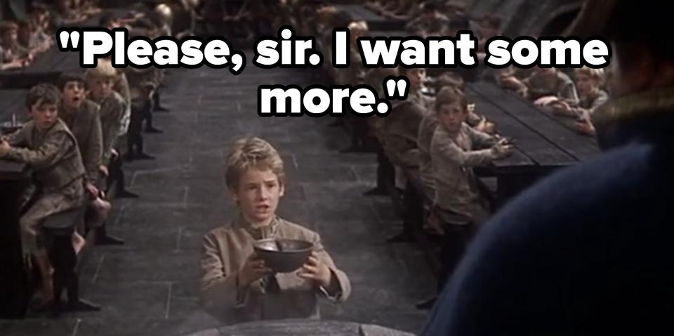 A boy in a crowded dining hall holds out his bowl to an adult, appearing to ask for more